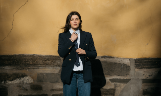 Behnaz Ganji står med jakke og slips  mot en gul vegg. 