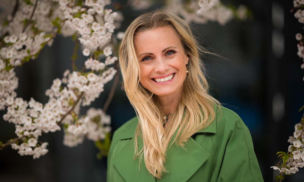 Silje Sandmæl står ute på gaten med trær som blomstrer.
