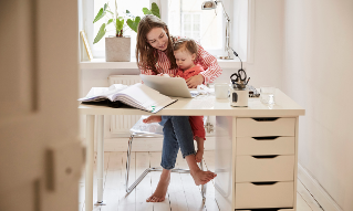 Female accountant sitting with daughter while working on laptop at home