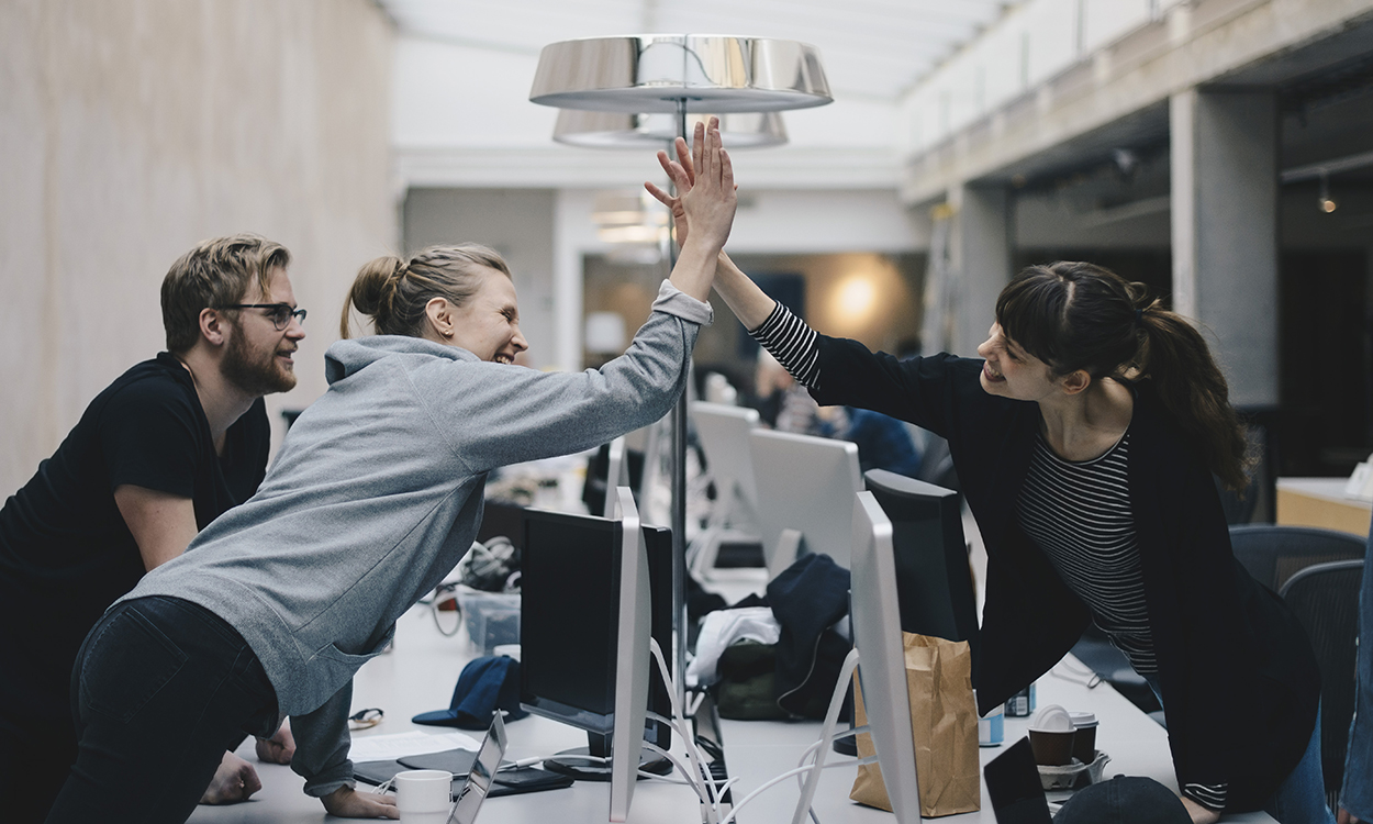 Happy female computer programmers giving high-five over desk in office