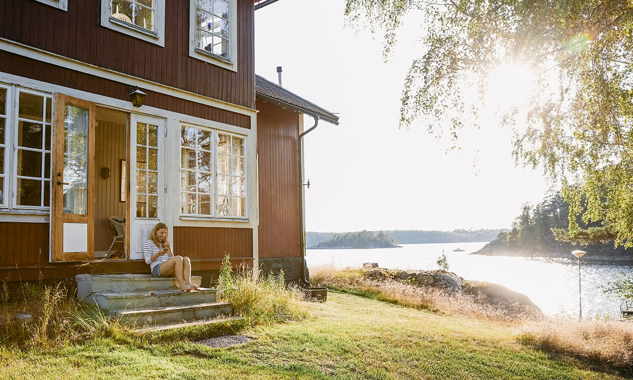 Jente sitter på en trapp utenfor en hytte ved sjøen