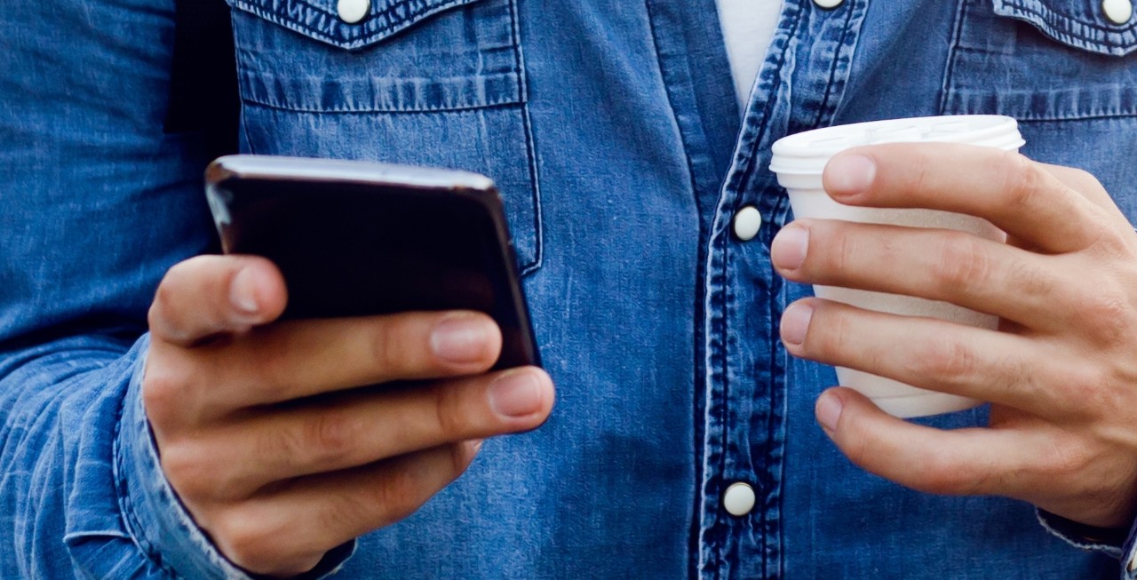 Mann titter på mobilen sin og drikker kaffe