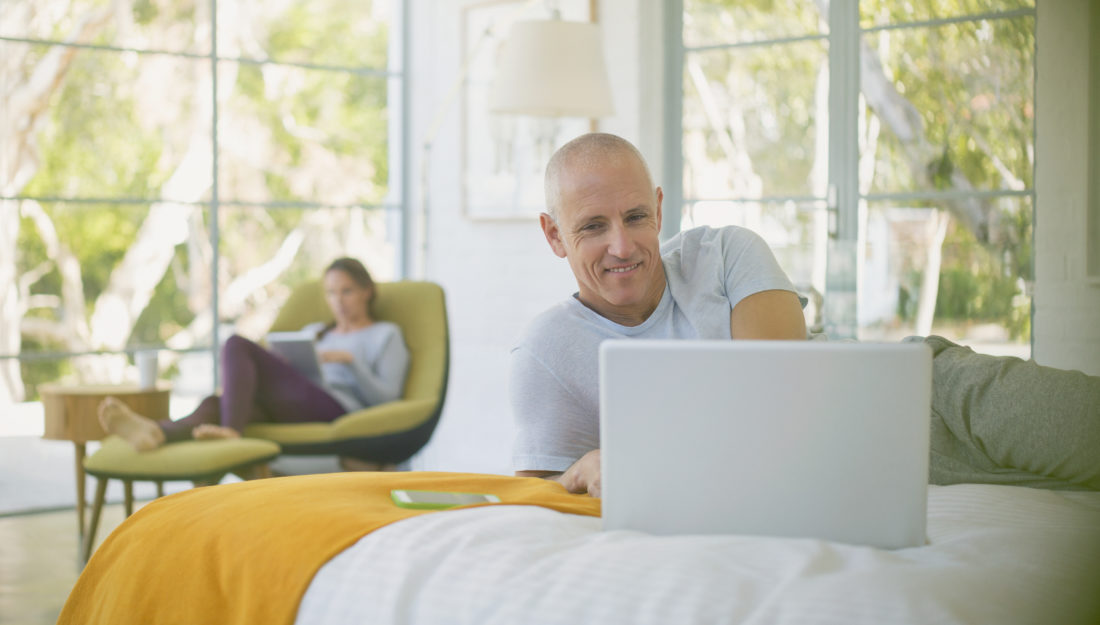 Mature couple relaxing, using laptop and digital tablet in bedroom.