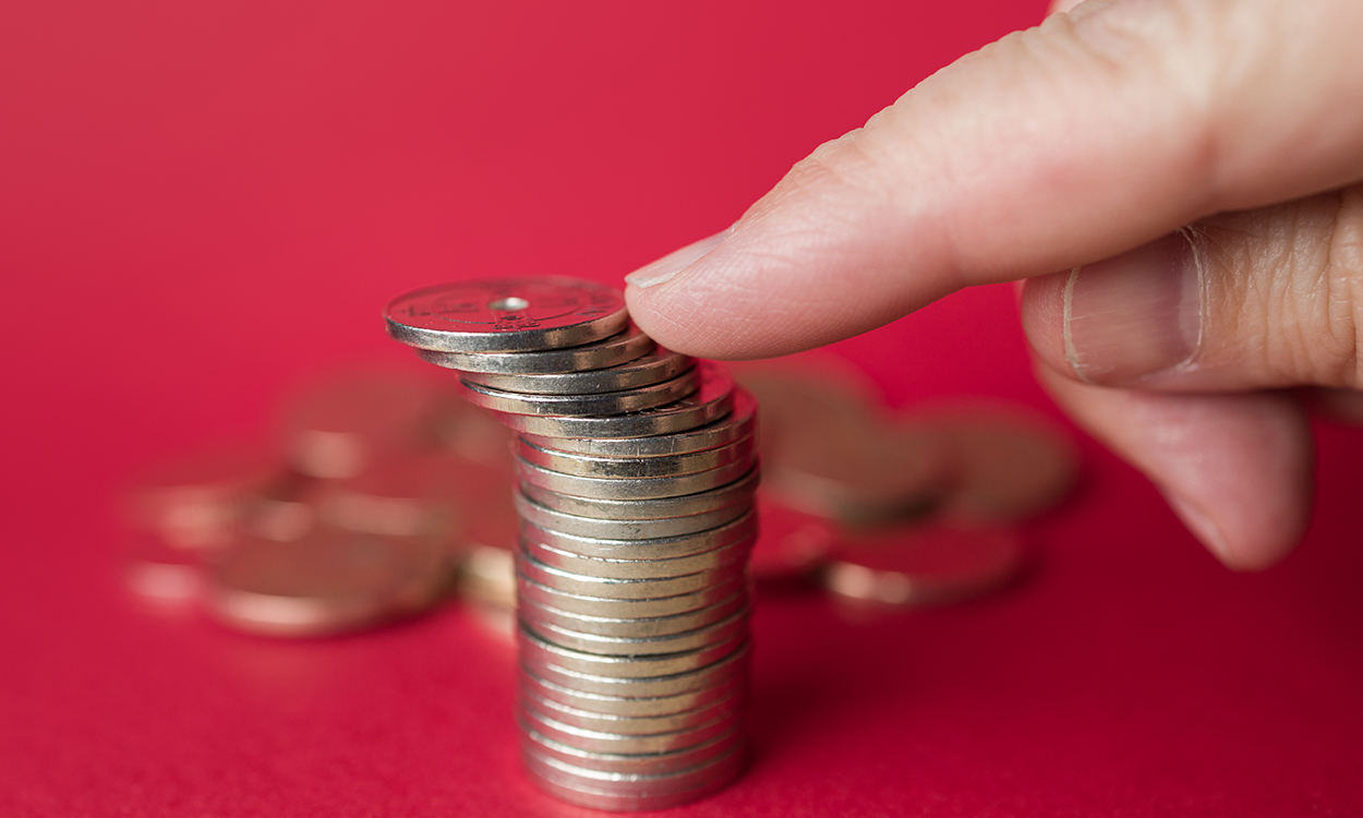 Illustrasjonsbilde av en stabel med norske enkroner på rød bakgrunn som dyttes ned med en pekefinger.