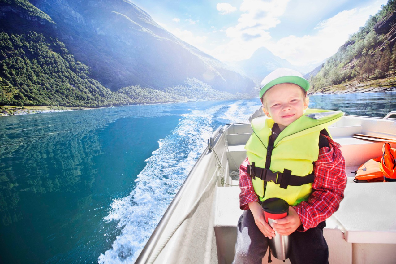 Boy is exploring fjord. The Geirangerfjord is unique and exceptionally beautiful â   which is why this fjord landscape is included on UNESCO's World Heritage List.