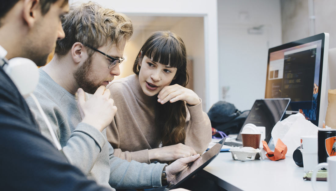 Male and female computer programmers discussing over digital tablet at desk in office