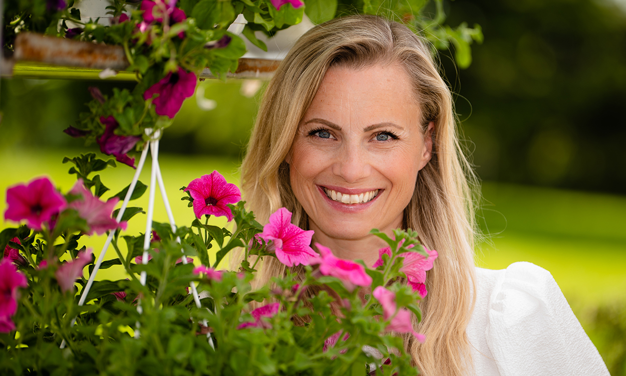Silje Sandmæl står ved flotte blomster som henger i krukker. 